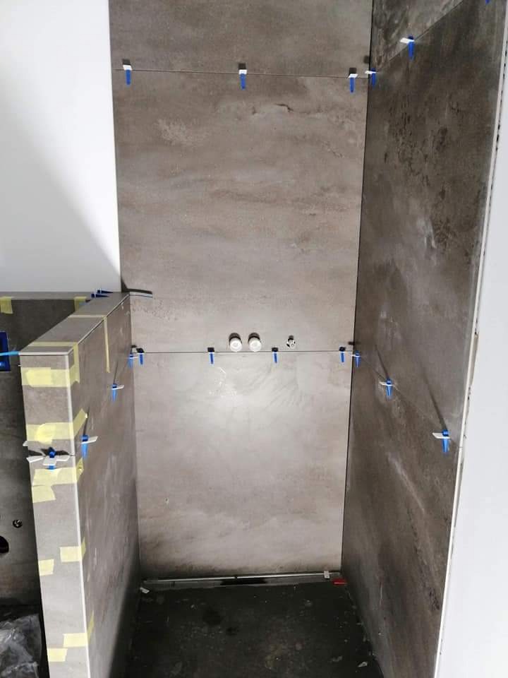 Ściany w trakcie układania płytek imitujących kamień, z użyciem niebieskich krzyżyków dystansowych i sznurka poziomującego; widoczne otwory na instalację wodną.