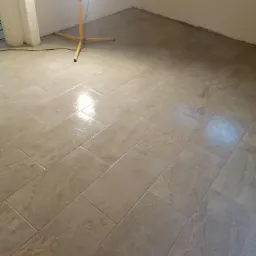 Ułożona pod kątem beżowa płytka podłogowa z widocznym oświetleniem roboczym na trójnogu w rogu pomieszczenia.