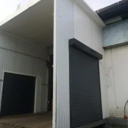 Zewnętrzna, stalowa rampa załadunkowa z zamontowaną czarną roletą zwijaną, częściowo opuszczoną.