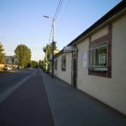 Budynek z beżową elewacją, oknami z kratami i ceglaną obramówką, widok z chodnika wzdłuż ulicy w słoneczny dzień.