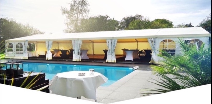 Biały namiot imprezowy z dekoracyjnymi zasłonami, ustawiony obok basenu, z małymi stolikami koktajlowymi wewnątrz i jednym stolikiem z białym obrusem na pierwszym planie.