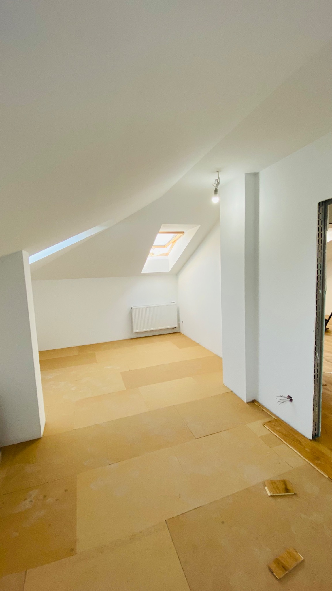 Poddasze z oknem dachowym, przygotowane do dalszych prac wykończeniowych, zabezpieczone kartonem, widoczny grzejnik i instalacja elektryczna