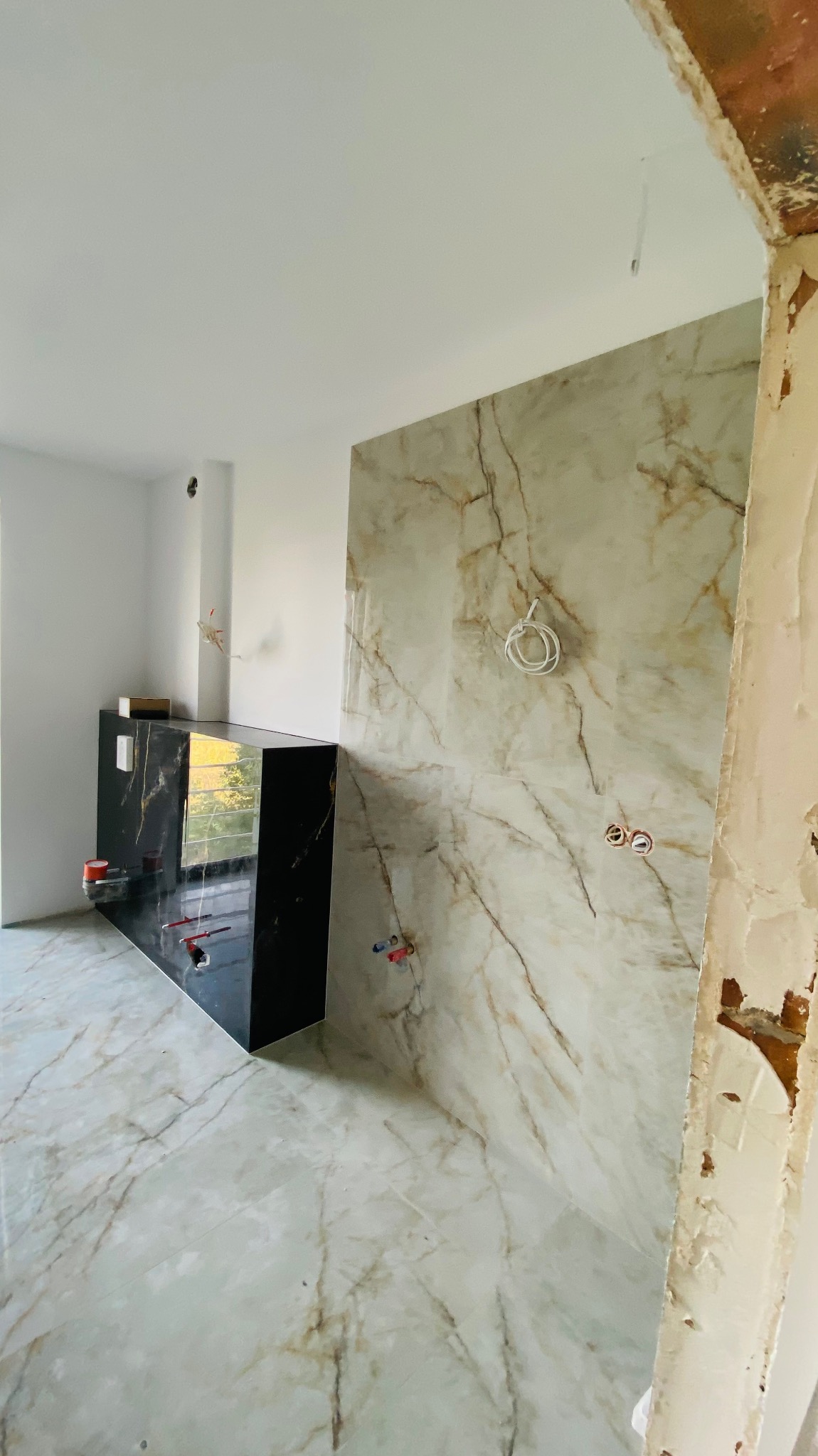 Łazienka w trakcie prac wykończeniowych: marmurowe płytki na ścianach i podłodze, czarna szafka umywalkowa z widocznymi instalacjami hydraulicznymi, surowy fragment ściany z odsłoniętą cegłą.