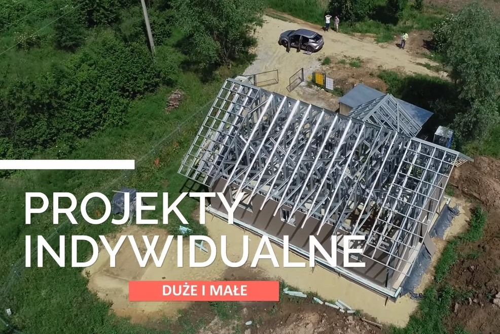 Widok z góry na konstrukcję stalową domu w trakcie budowy, z widocznym szkieletem dachu, samochodem i osobami w tle.