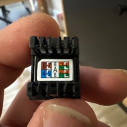 Instal-Tech Szymon Waszak - Złącze RJ45 w dłoni, widoczne oznaczenia kolorystyczne i numeryczne pinów. Detal z bliska, ukazujący precyzję montażu sieci komputerowej.