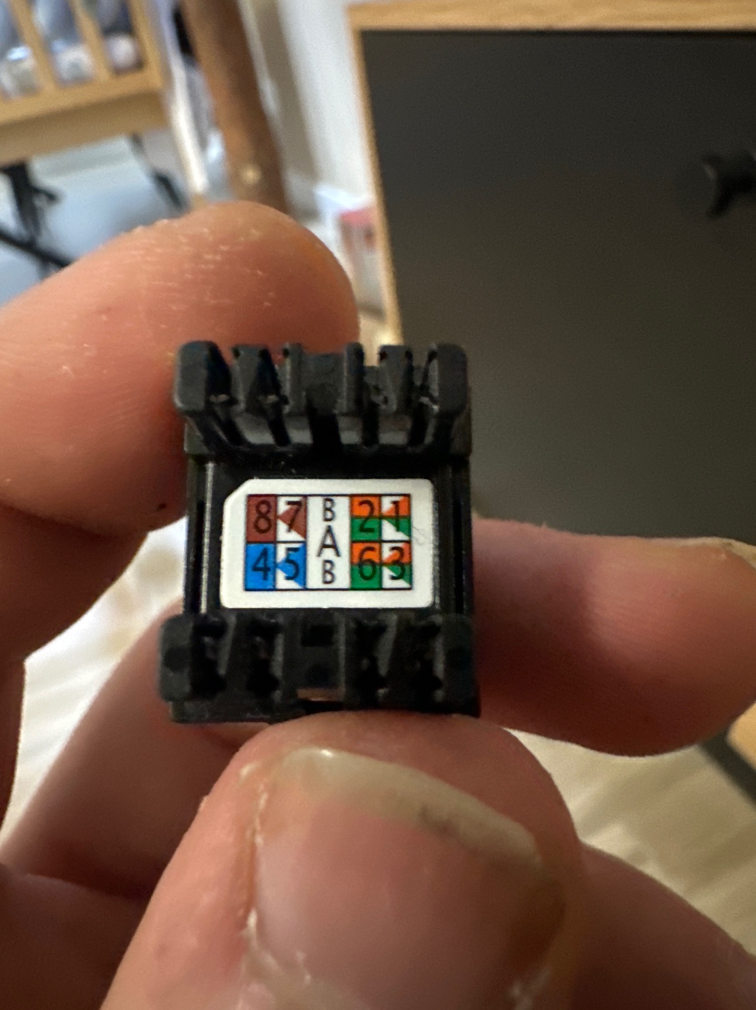 Złącze RJ45 w dłoni, widoczne oznaczenia kolorystyczne i numeryczne pinów. Detal z bliska, ukazujący precyzję montażu sieci komputerowej.