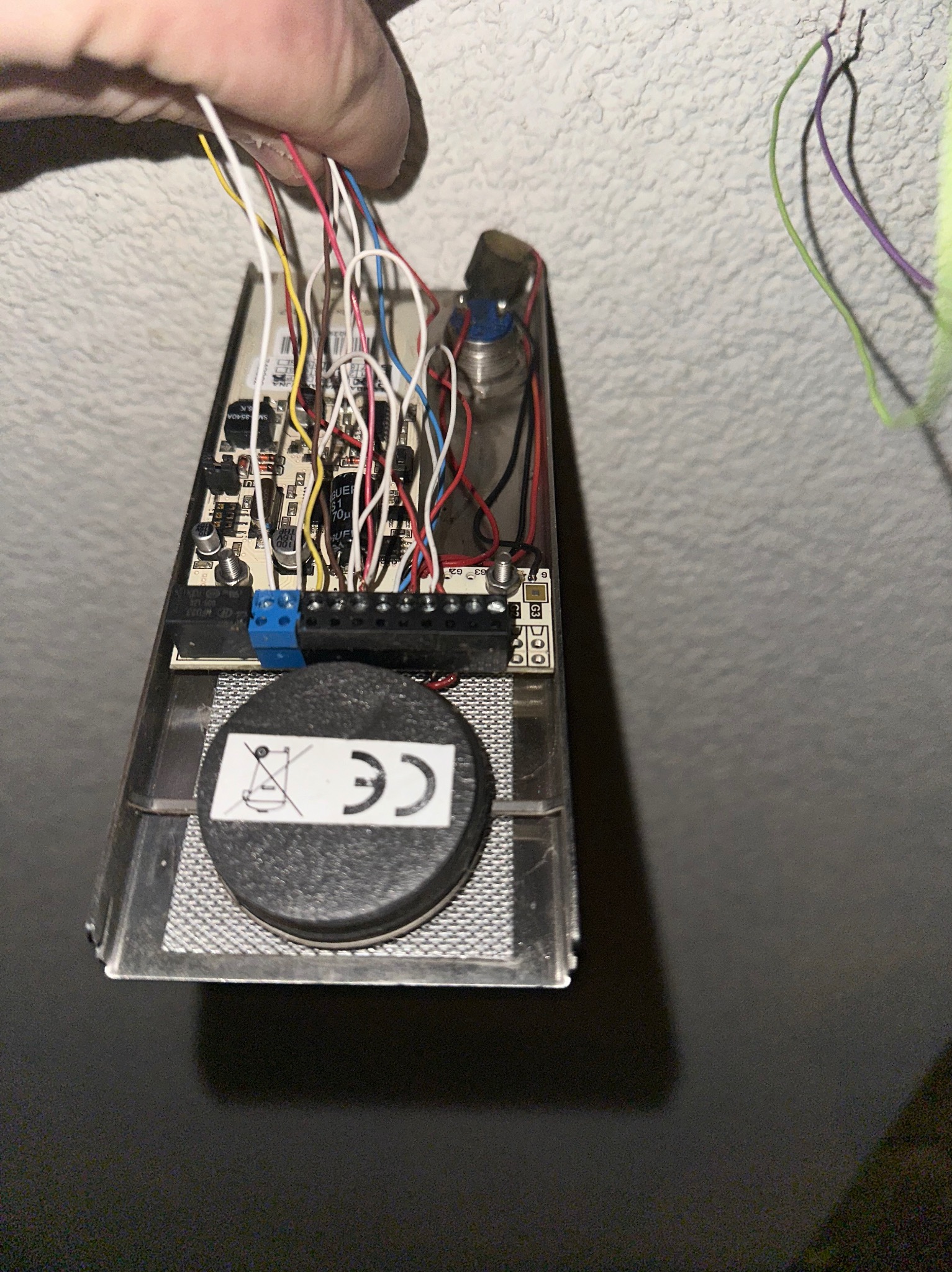 Otwarta obudowa czujnika alarmowego z widoczną elektroniką, podłączonymi przewodami i elementami montażowymi. Widoczne oznaczenia CE na elemencie czujnika.