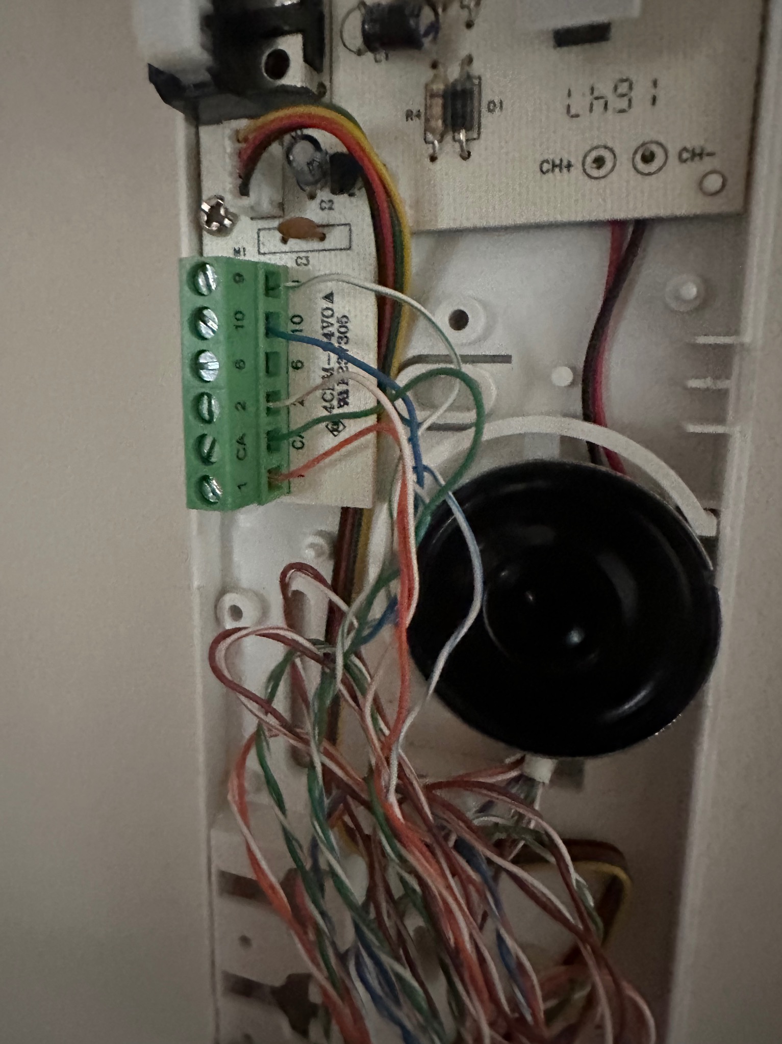 Wnętrze rozmontowanego domofonu z widocznymi przewodami, złączami i elementami elektroniki. Detal złącza śrubowego z podłączonymi przewodami w różnych kolorach.