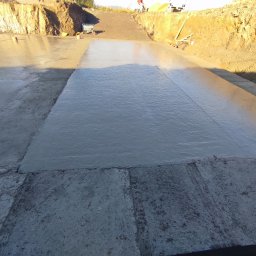 Perbud - Świeżo wylany beton na fundamencie, widoczne ślady po narzędziach i zagłębienia w ziemi.