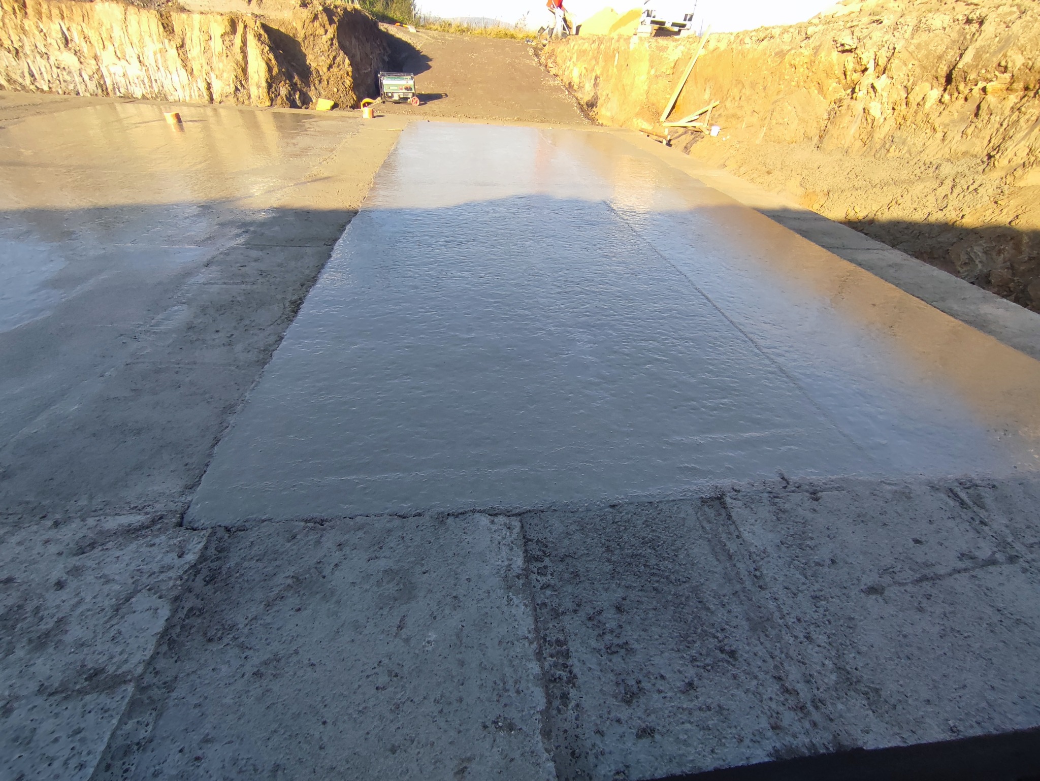 Świeżo wylany beton na fundamencie, widoczne ślady po narzędziach i zagłębienia w ziemi.