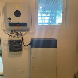 VIMA Energia Sp. z o.o. - Wewnętrzna instalacja fotowoltaiczna: falownik Fronius SYMO, rozdzielnica PV-DC marki ETI oraz moduł magazynu energii BYD Premium LVL, zamontowane na ścianie w pomieszczeniu z oknem.