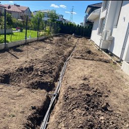 WK SERWIS - Montaż systemu nawadniania w ogrodzie: wykopane rowy z ułożonymi rurami, widok z góry, dom w tle.