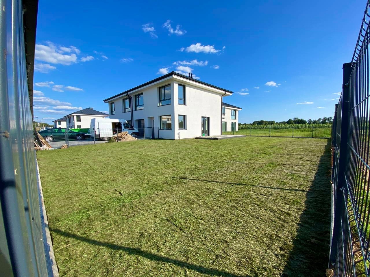 Nowo założony trawnik z rolki przed nowoczesnym domem jednorodzinnym w słoneczny dzień, widok zza ogrodzenia.