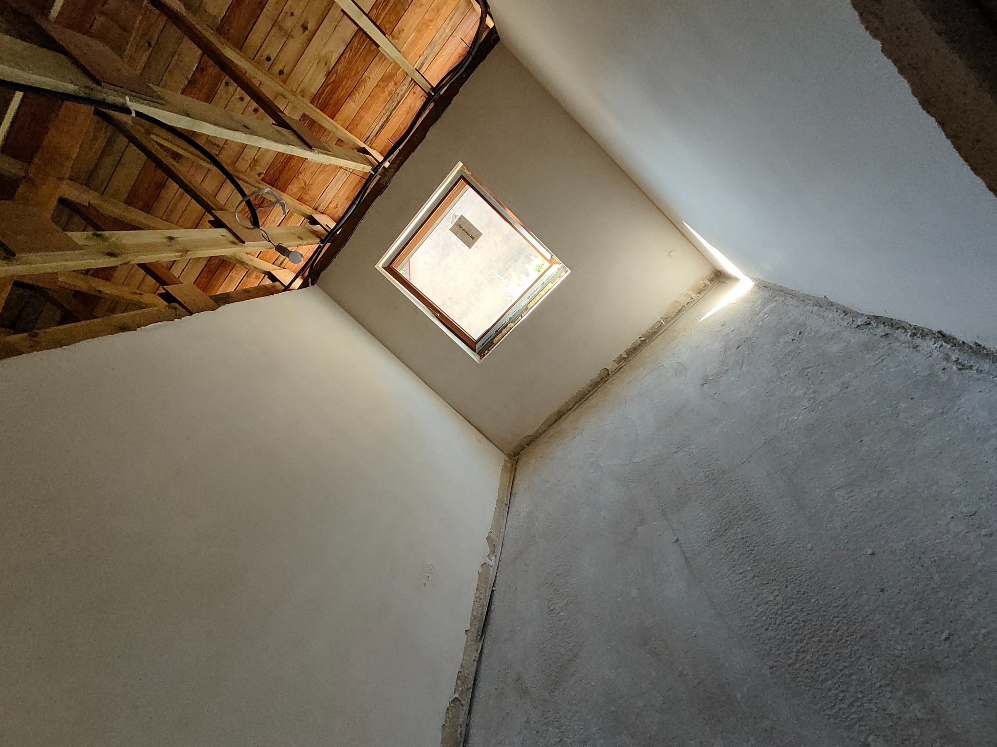 Wnętrze poddasza w Sulechowie w trakcie prac wykończeniowych, widoczne surowe tynki i konstrukcja dachu z oknem połaciowym.