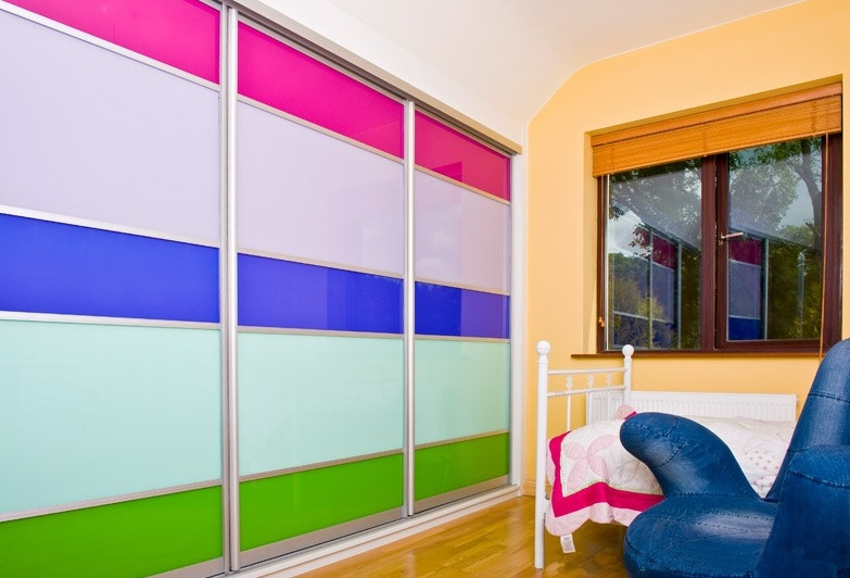 Kolorowa szafa przesuwna z panelami w odcieniach różu, fioletu, niebieskiego, zieleni w pokoju dziecięcym z łóżkiem i fotelem.