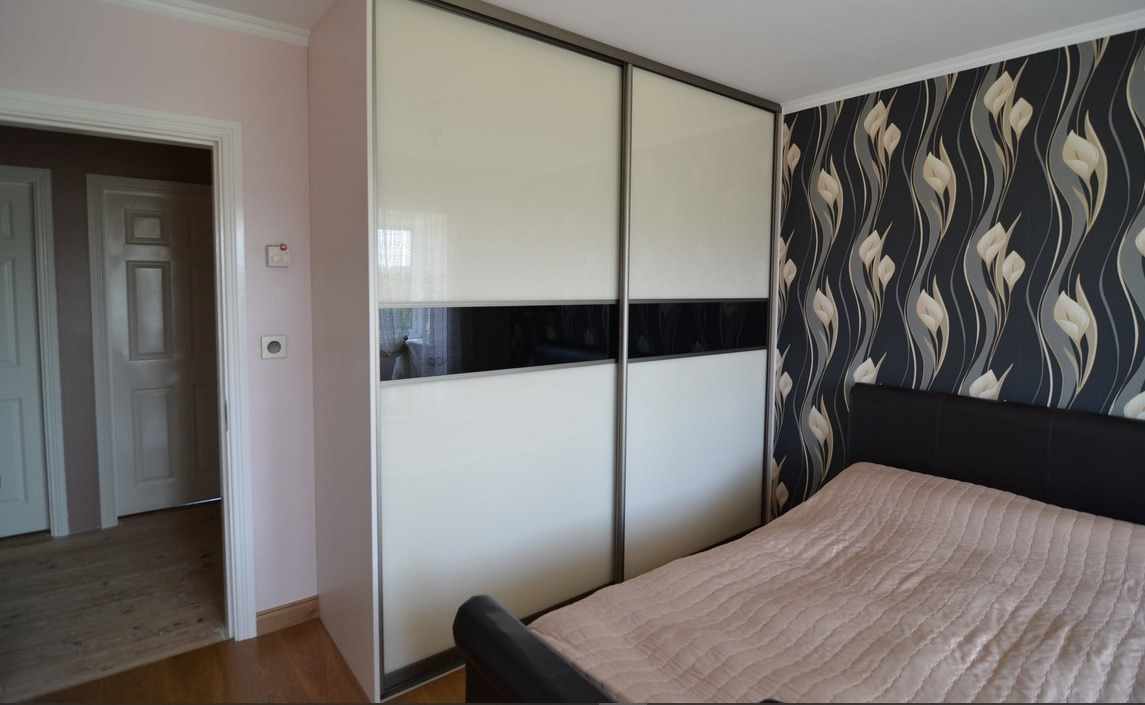 Dwudrzwiowa szafa przesuwna z białymi i czarnymi panelami w sypialni z wzorzystą tapetą i widocznym łóżkiem.