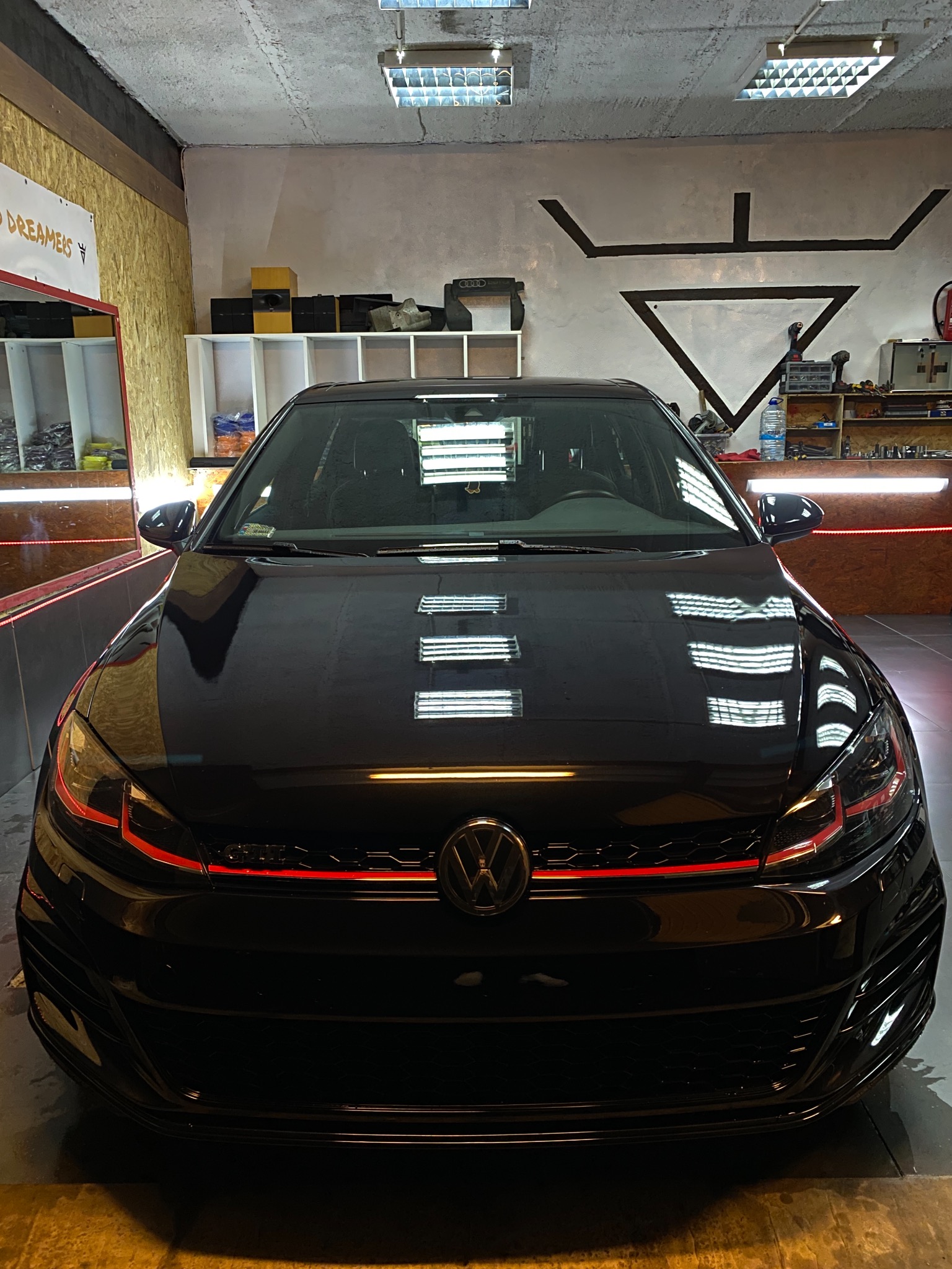 Czarny Volkswagen Golf GTI w garażu z betonową podłogą, widoczne odbicia światła na karoserii i czerwone akcenty na przednim grillu.