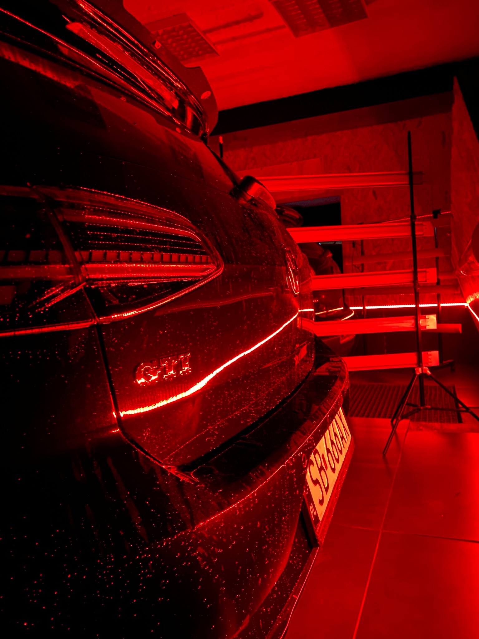 Czarny samochód GTI poddawany suszeniu lakieru lampami na podczerwień w czerwonym oświetleniu myjni.