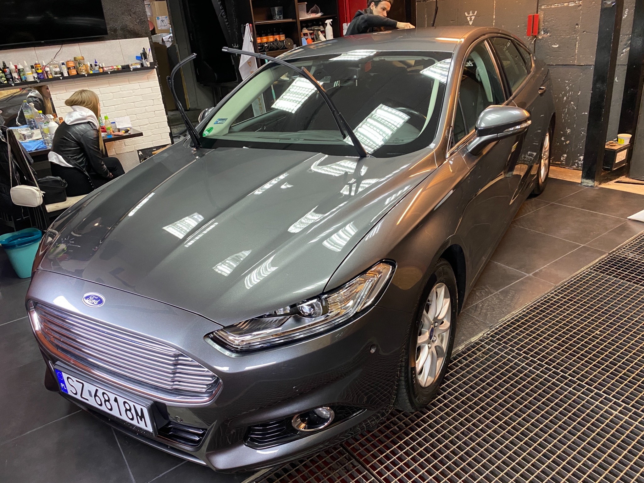 Szary Ford Mondeo po umyciu, stojący na metalowej kratce w myjni, z podniesionymi wycieraczkami i widoczną rejestracją SZ 6818M.