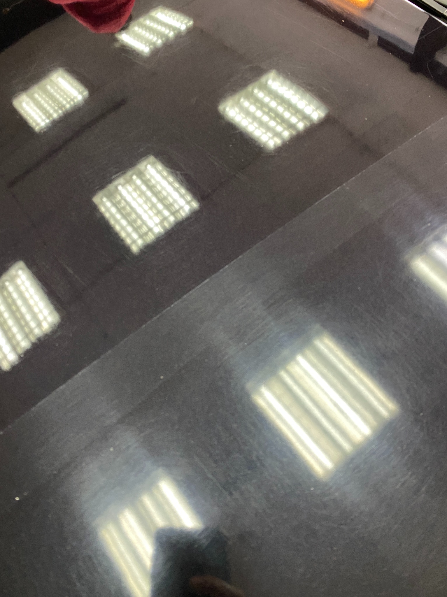 Częściowo wypolerowana, czarna karoseria samochodu z widocznymi odbiciami lamp sufitowych i śladami po polerowaniu, ukazująca różnicę przed i po zabiegu.