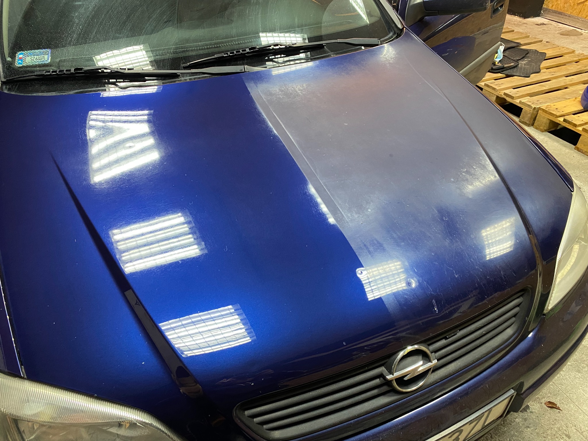 Niebieski samochód z widoczną różnicą w połysku lakieru na masce, ukazując obszar po polerowaniu.