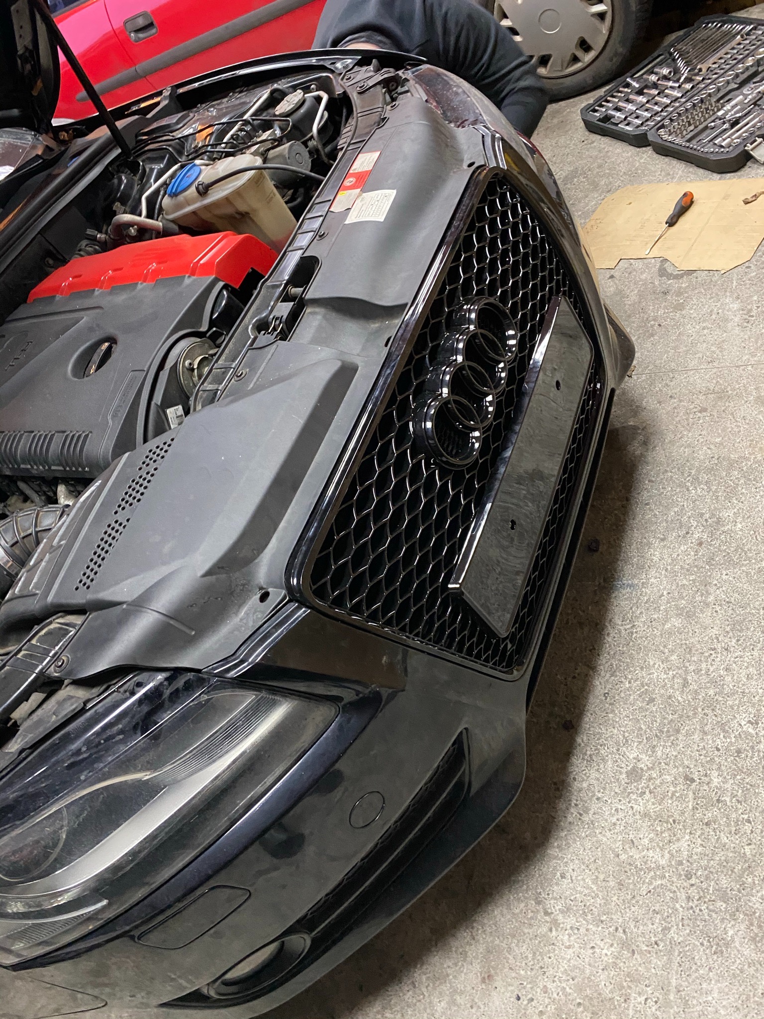 Czarny samochód marki Audi z otwartą maską, widoczny silnik oraz zestaw narzędzi obok, sugerujący prace serwisowe.