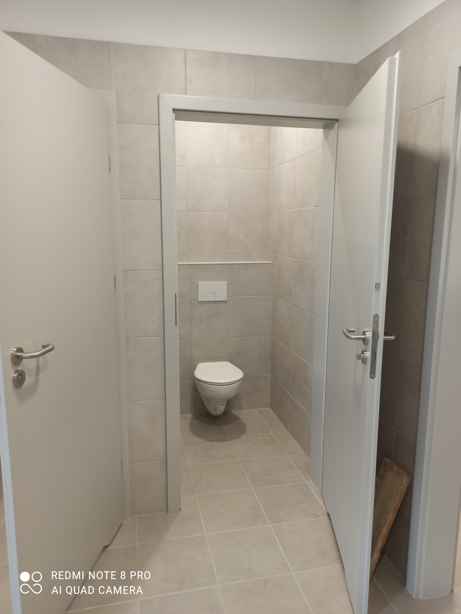 Wykończona łazienka w Dębnie z beżowymi płytkami na ścianach i podłodze, widoczna toaleta wisząca i dwie białe ościeżnice drzwiowe z otwartymi drzwiami.