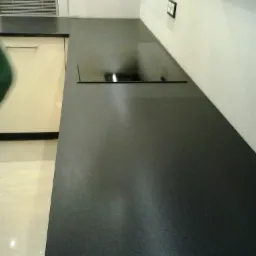 Ciemny, błyszczący blat z wbudowaną płytą grzewczą, widok z perspektywy, z elementami zabudowy kuchennej i gniazdkiem elektrycznym na ścianie.