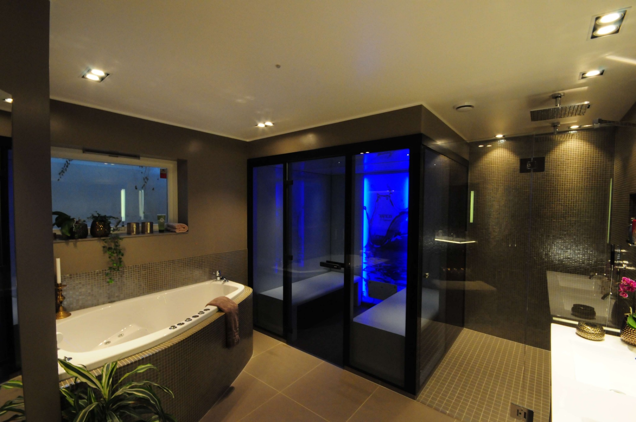 Nowoczesna łazienka z wanną z hydromasażem, kabiną prysznicową z mozaiką i sauną z niebieskim oświetleniem.