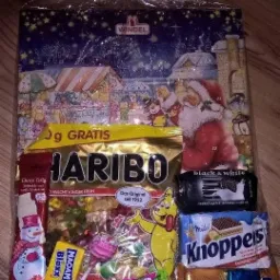 Foliowy worek prezentowy z motywem bożonarodzeniowym, wypełniony słodyczami, w tym Haribo, Knoppers, Black&White i lizakami, leżący na drewnianej powierzchni.