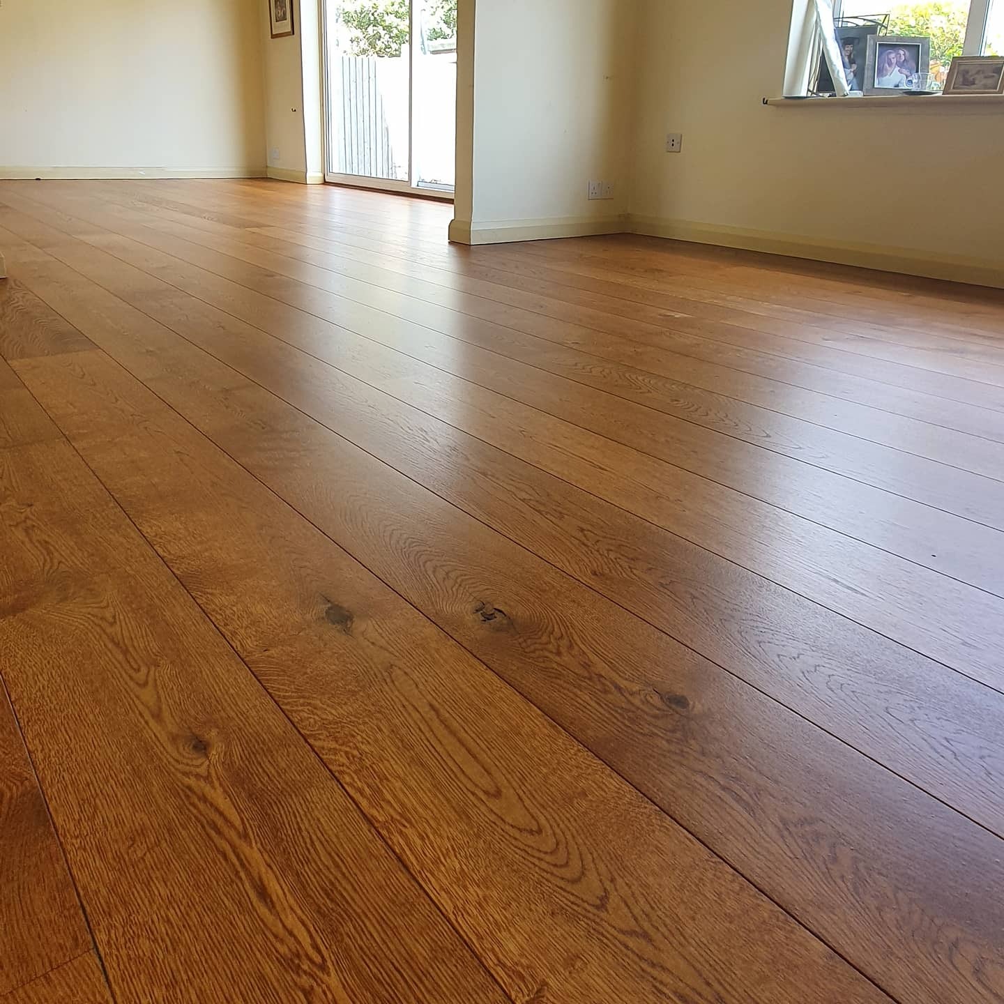 Nowo ułożona, lakierowana podłoga z desek parkietowych w jasnym, pustym pokoju z przesuwnymi drzwiami balkonowymi i oknem z ramkami na parapecie.