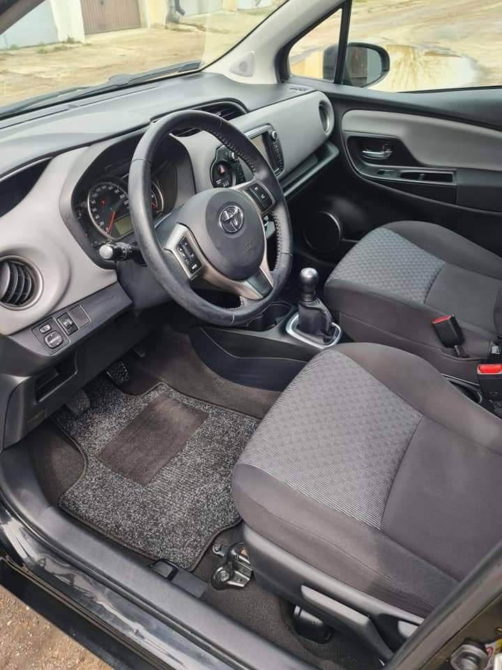 Wnętrze samochodu Toyota Yaris po czyszczeniu: widoczne odkurzone dywaniki, czyste fotele z szarej tapicerki i kokpit. Kierownica z logo Toyota.