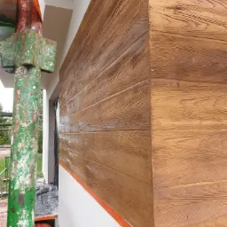 Fragment elewacji budynku z nową, brązową powłoką imitującą drewno, widoczna z bliska z rusztowaniem w lewym dolnym rogu, na dole pomarańczowa taśma zabezpieczająca.