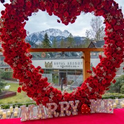 Balony Happy Day Zakopane - Romantyczna sceneria zaręczyn w Zakopanem: serce z czerwonych róż i białych gipsówek, podświetlany napis 'MARRY ME', świece, czerwony dywan, w tle budynek Royal Resort Wellness & Spa oraz ośnieżone...