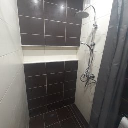 ES-BUD Eryk Szczerbowski - Kabina prysznicowa z chromowaną armaturą, wykończona płytkami w odcieniach brązu i beżu, z szarą zasłoną prysznicową.