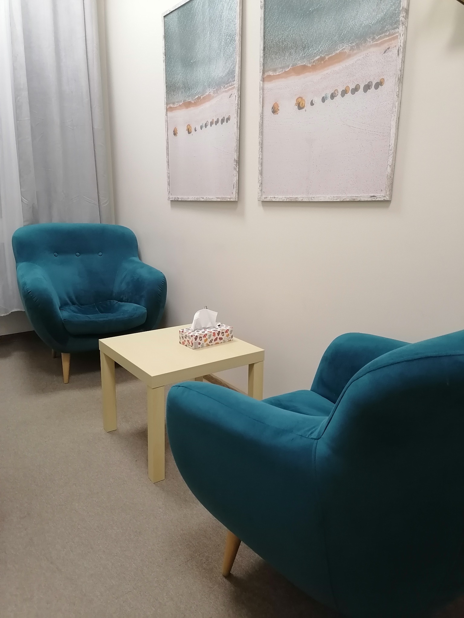 Gabinet z dwoma turkusowymi fotelami, stolikiem z chusteczkami i obrazami plaży na ścianie.