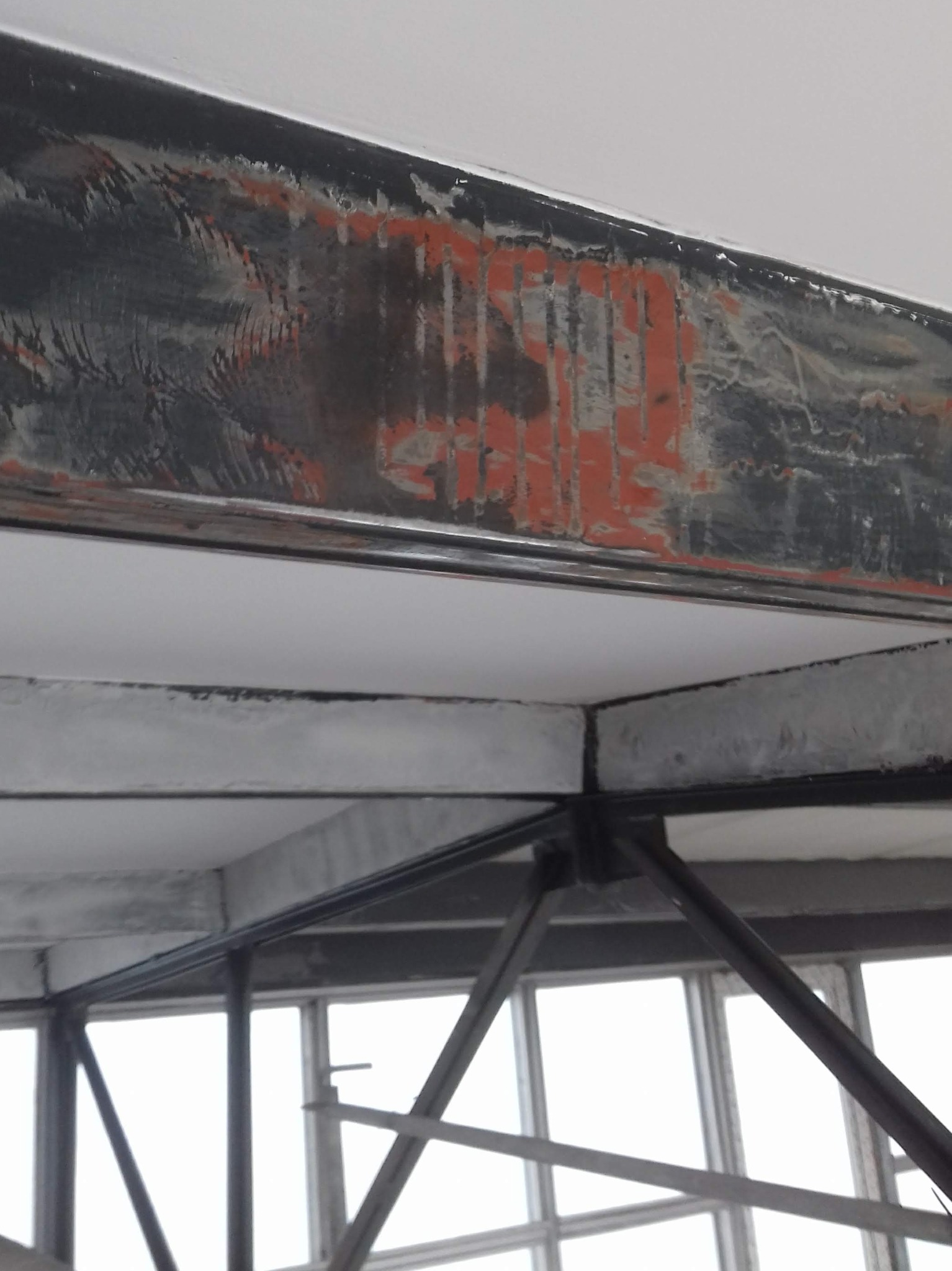 Stalowa konstrukcja stropu z widocznymi śladami rdzy i starej farby na belkach, surowy industrialny wygląd wnętrza.