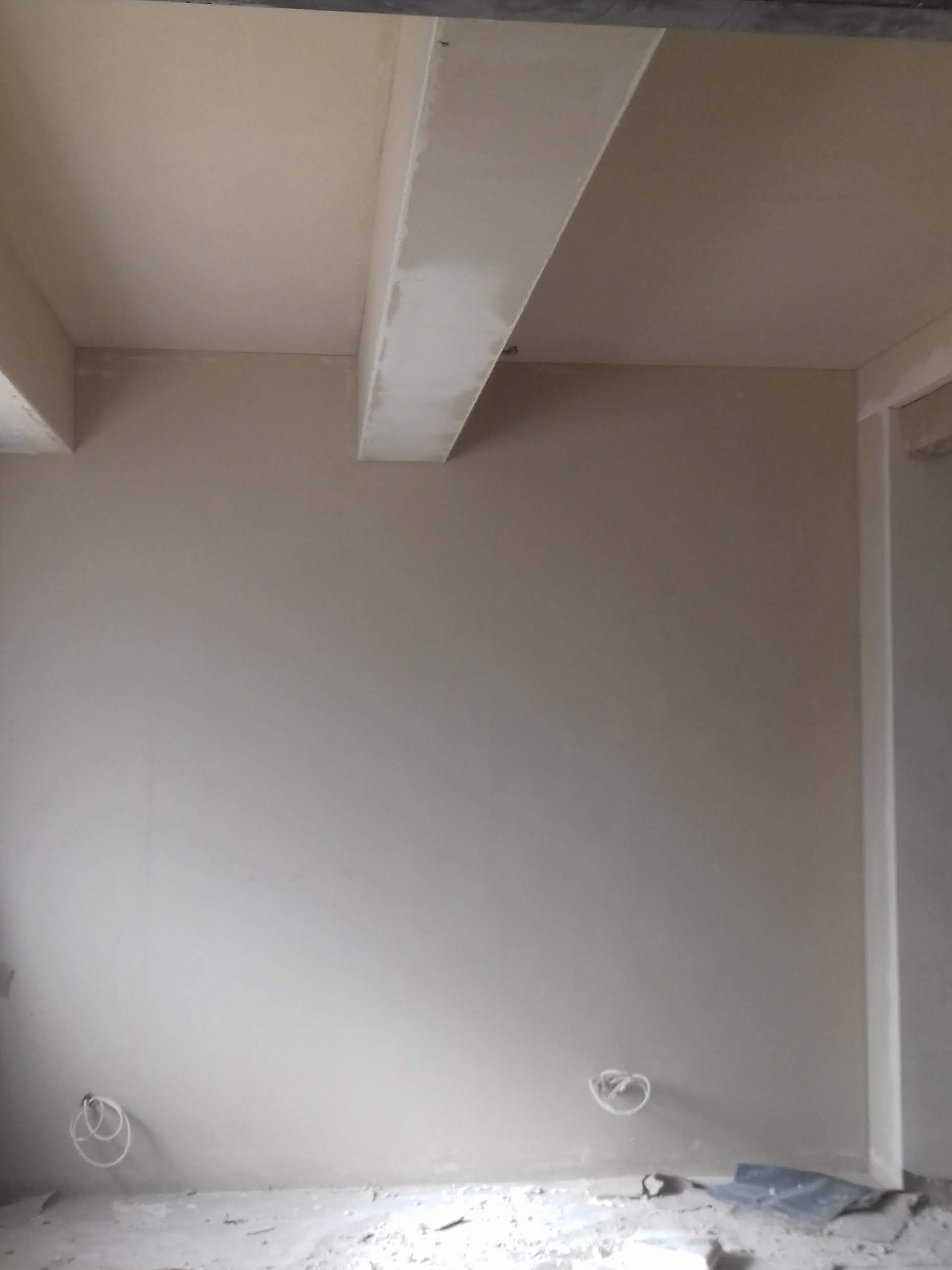 Wnętrze w trakcie prac wykończeniowych: gładkie, beżowe ściany, widoczne kable elektryczne wystające ze ściany, surowy sufit z elementami konstrukcyjnymi.