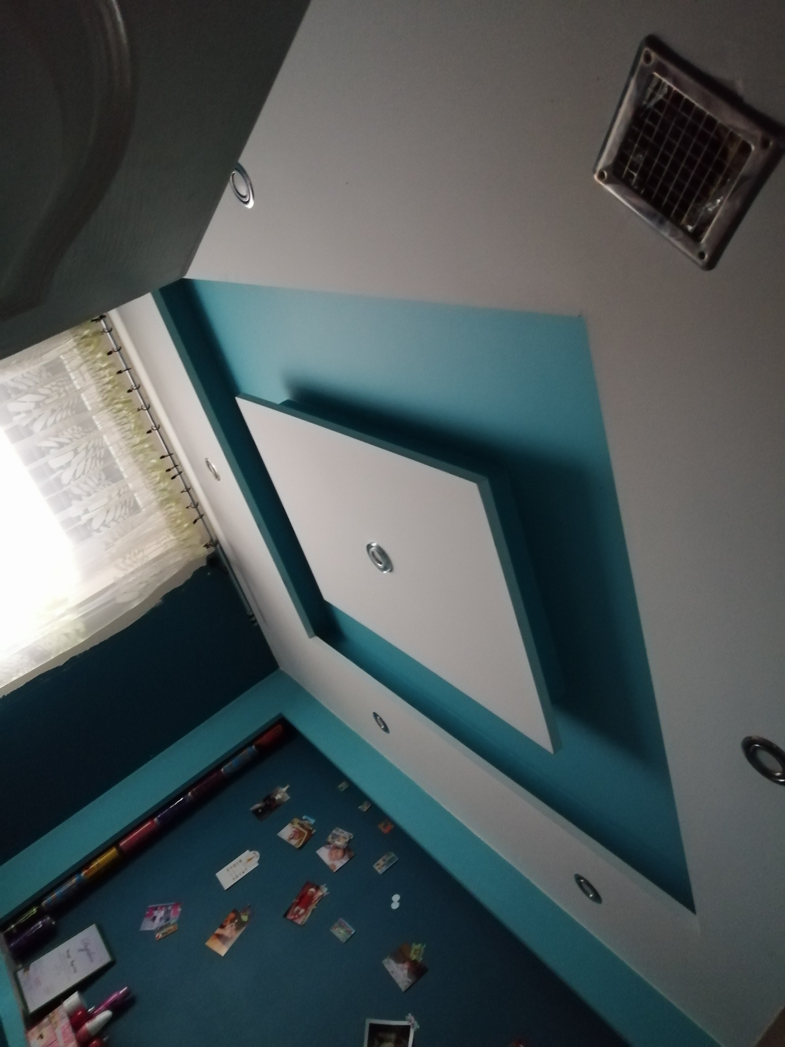 Nowoczesny sufit podwieszany z oświetleniem punktowym i turkusowymi akcentami, widok z dołu ukazujący detale wykończenia i wentylację.