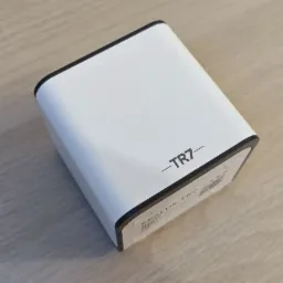 Biała centralka inteligentnego domu TR7 z czarnymi krawędziami, leżąca na jasnym drewnianym blacie, widok z góry pod kątem.