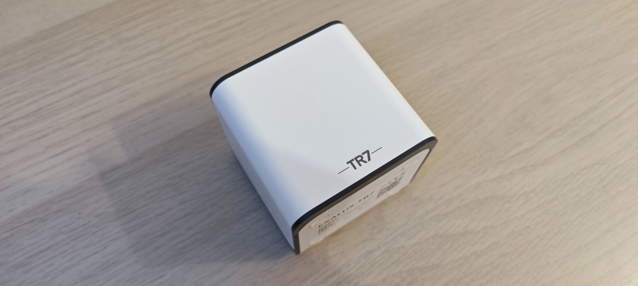 Biała centralka inteligentnego domu TR7 z czarnymi krawędziami, leżąca na jasnym drewnianym blacie, widok z góry pod kątem.