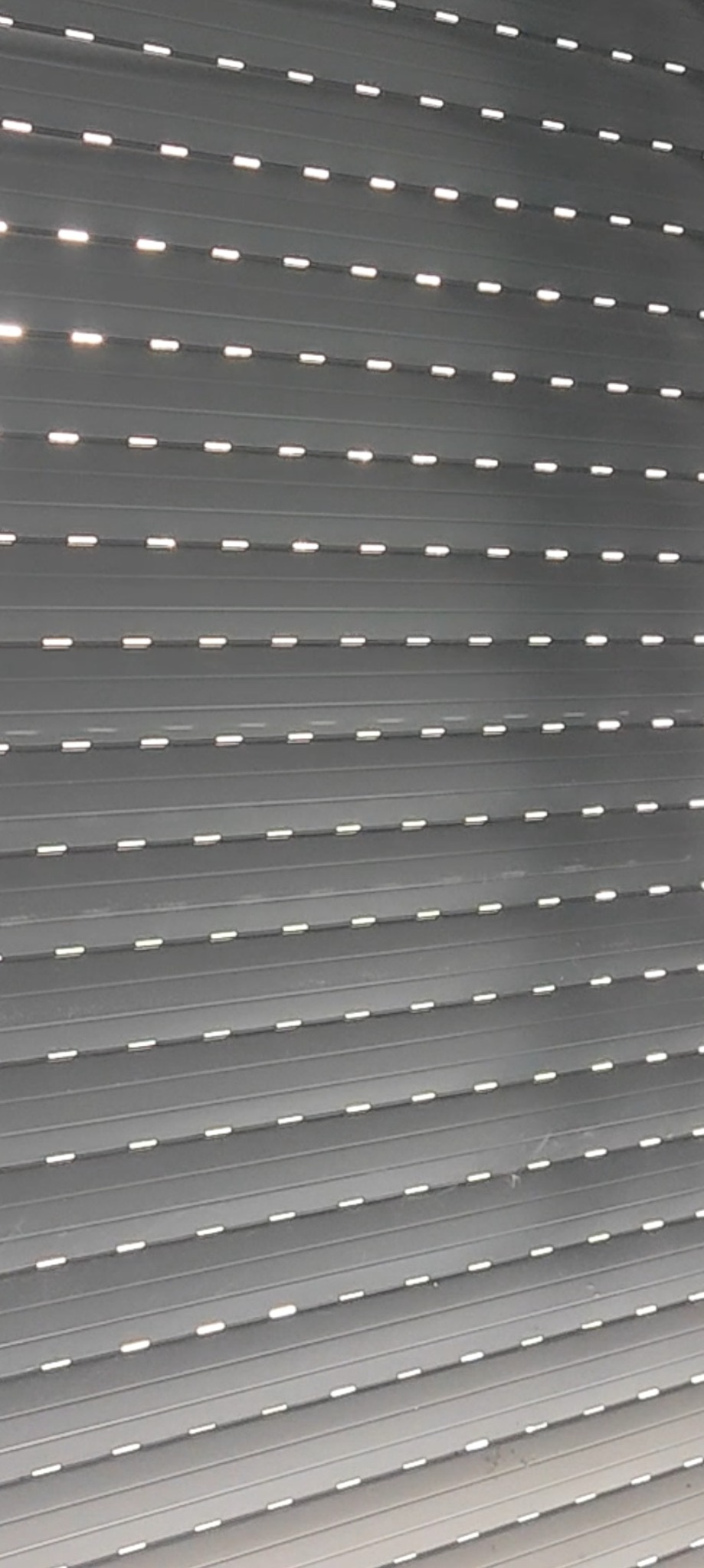 Szare rolety zewnętrzne z poziomymi lamelami i niewielkimi otworami przepuszczającymi światło.