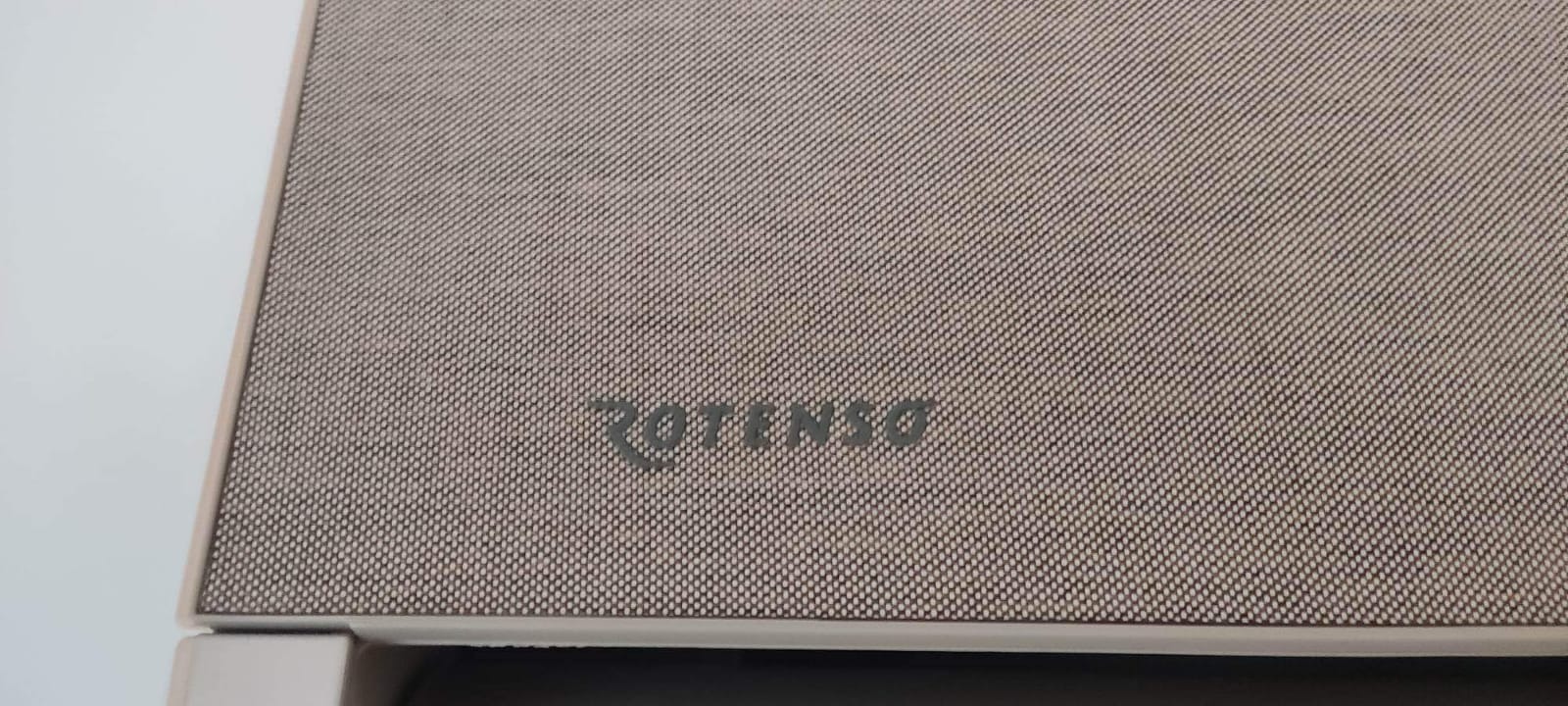 Fragment klimatyzatora z widocznym logo 'Rotenso' na teksturowanej obudowie w odcieniach szarości.