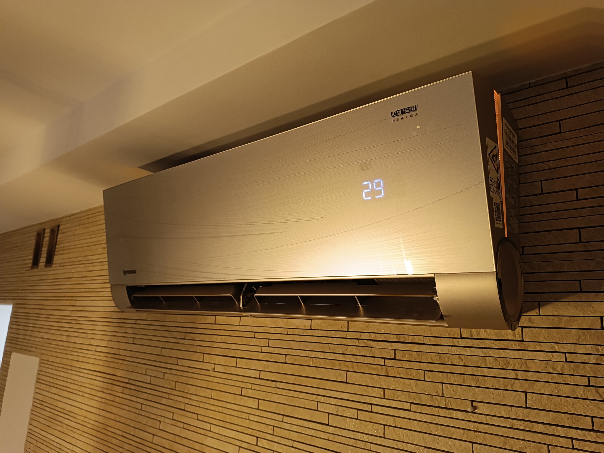 Zamontowana klimatyzacja ścienna Versui Series z wyświetlaną temperaturą 29 stopni Celsjusza, zainstalowana na ścianie z dekoracyjnej cegły.