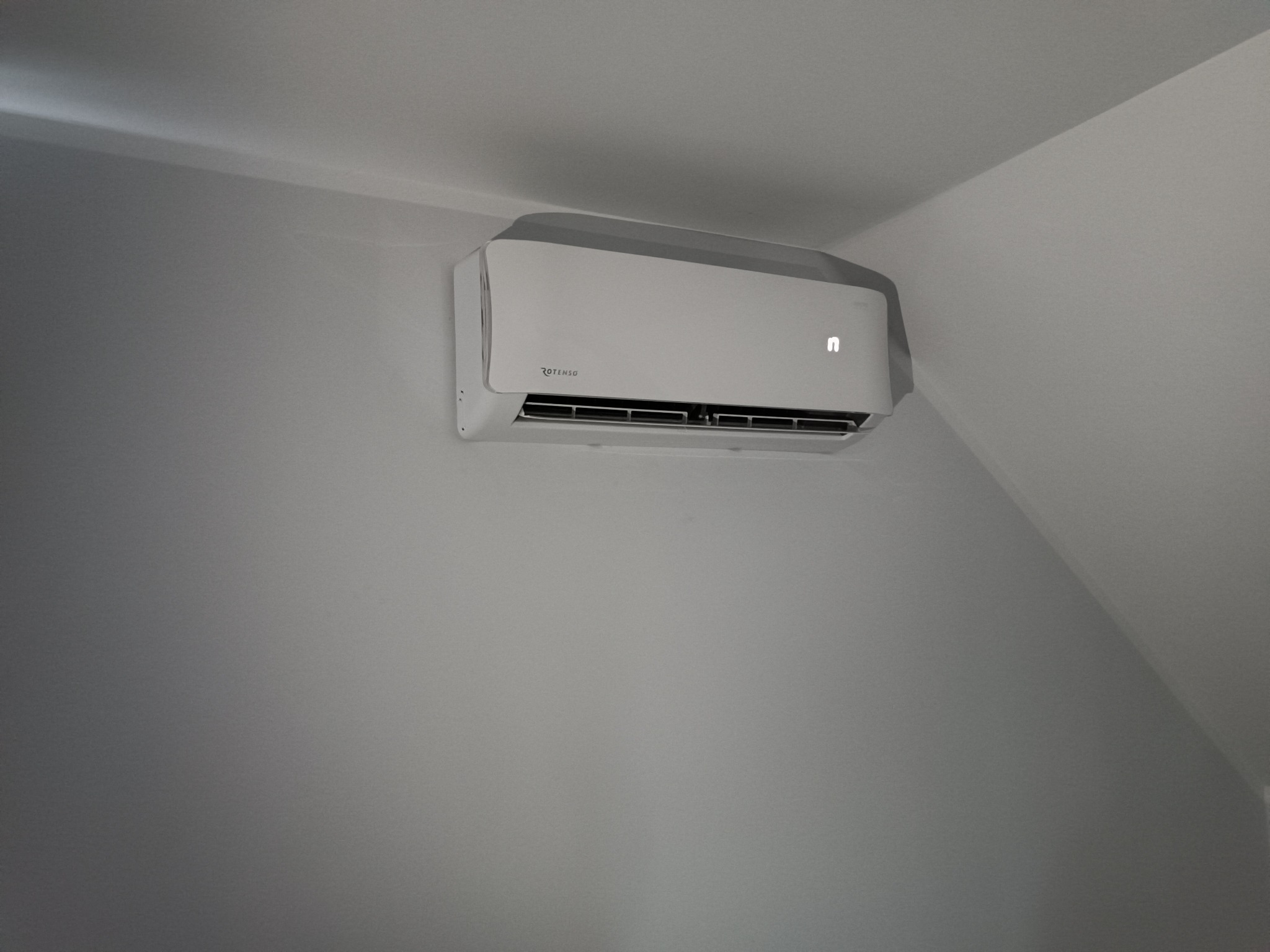 Biały klimatyzator Rotenso zamontowany na ścianie w jasnym pomieszczeniu, widoczny wyświetlacz z literą 'n'.