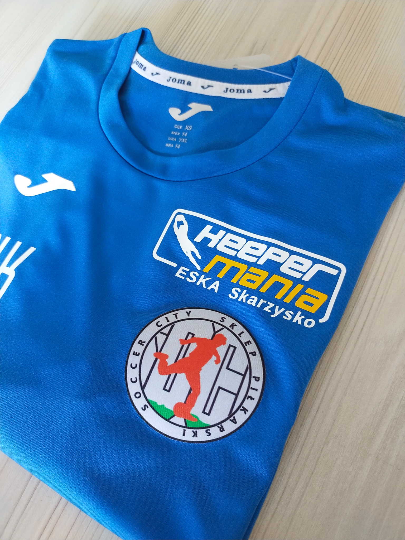 Niebieska koszulka sportowa z nadrukowanymi logotypami i napisami, w tym 'Heeper Mania ESKA Skarzysko' oraz logo klubu piłkarskiego z piłkarzem.