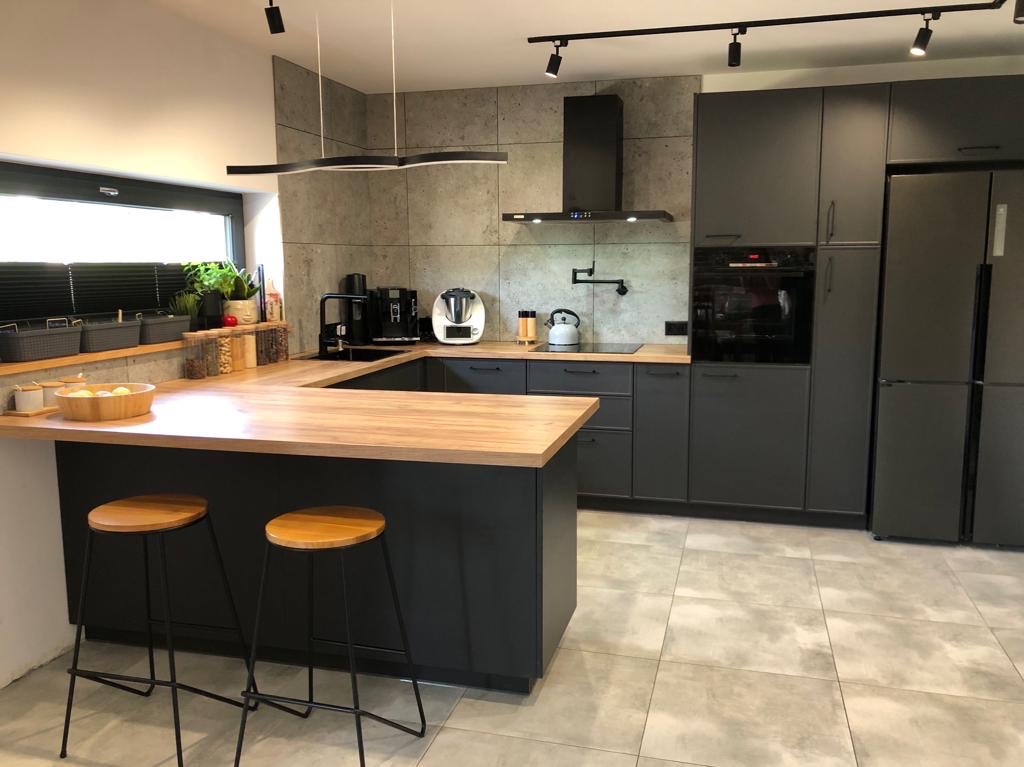 Nowoczesna kuchnia w odcieniach szarości z drewnianym blatem, oświetleniem punktowym i dwoma hokerami przy wyspie.