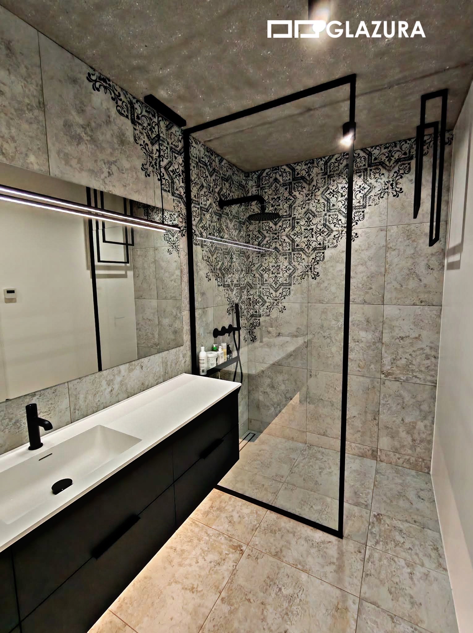Nowoczesna łazienka z kabiną typu walk-in, umywalką nablatową i płytkami imitującymi beton, akcentowana czarnymi elementami i dekoracyjnym wzorem na ścianie.