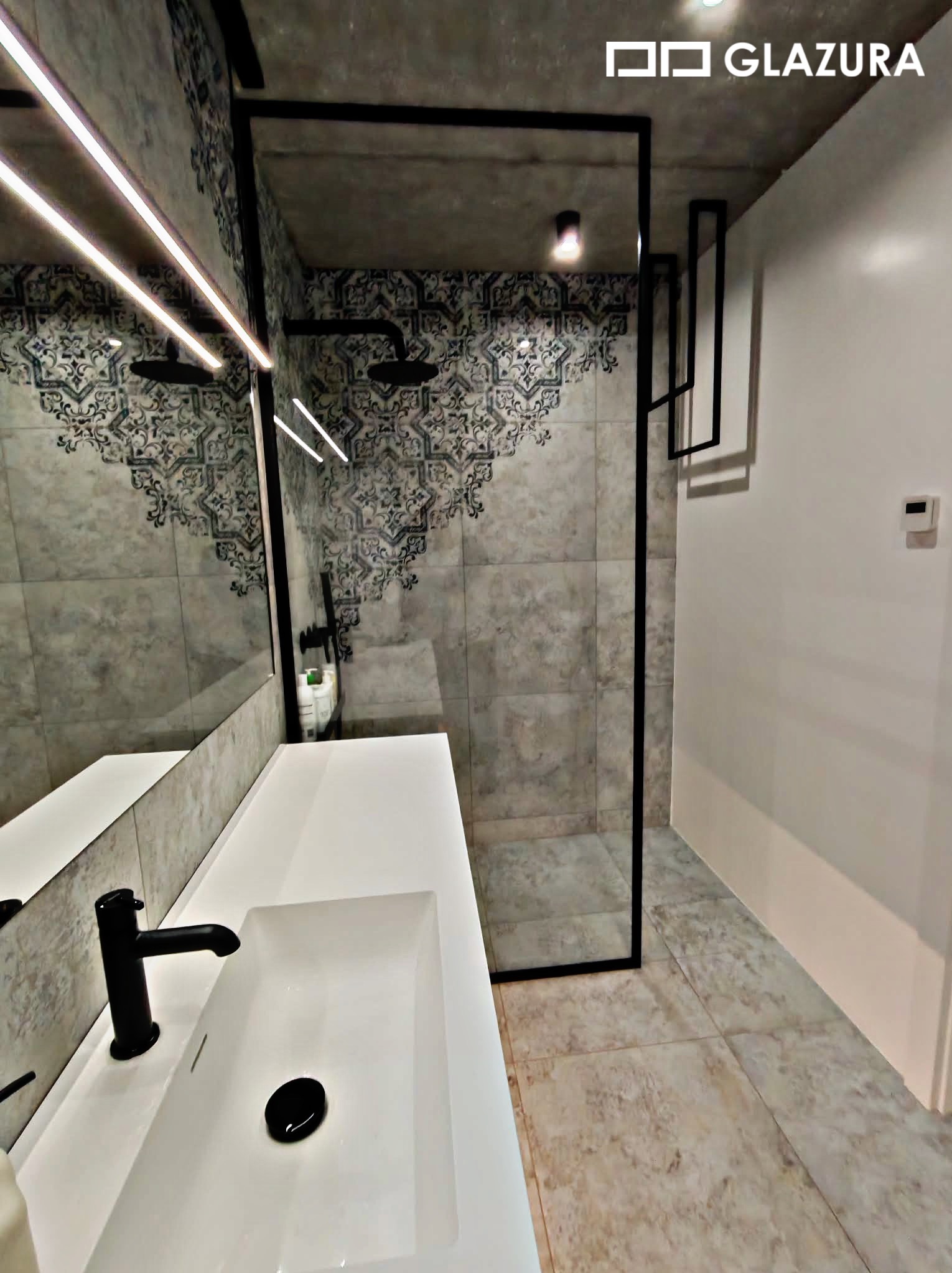 Nowoczesna łazienka z kabiną prysznicową typu walk-in, białą umywalką nablatową i dekoracyjnymi płytkami w strefie prysznica. Minimalistyczny design z czarnymi akcentami.