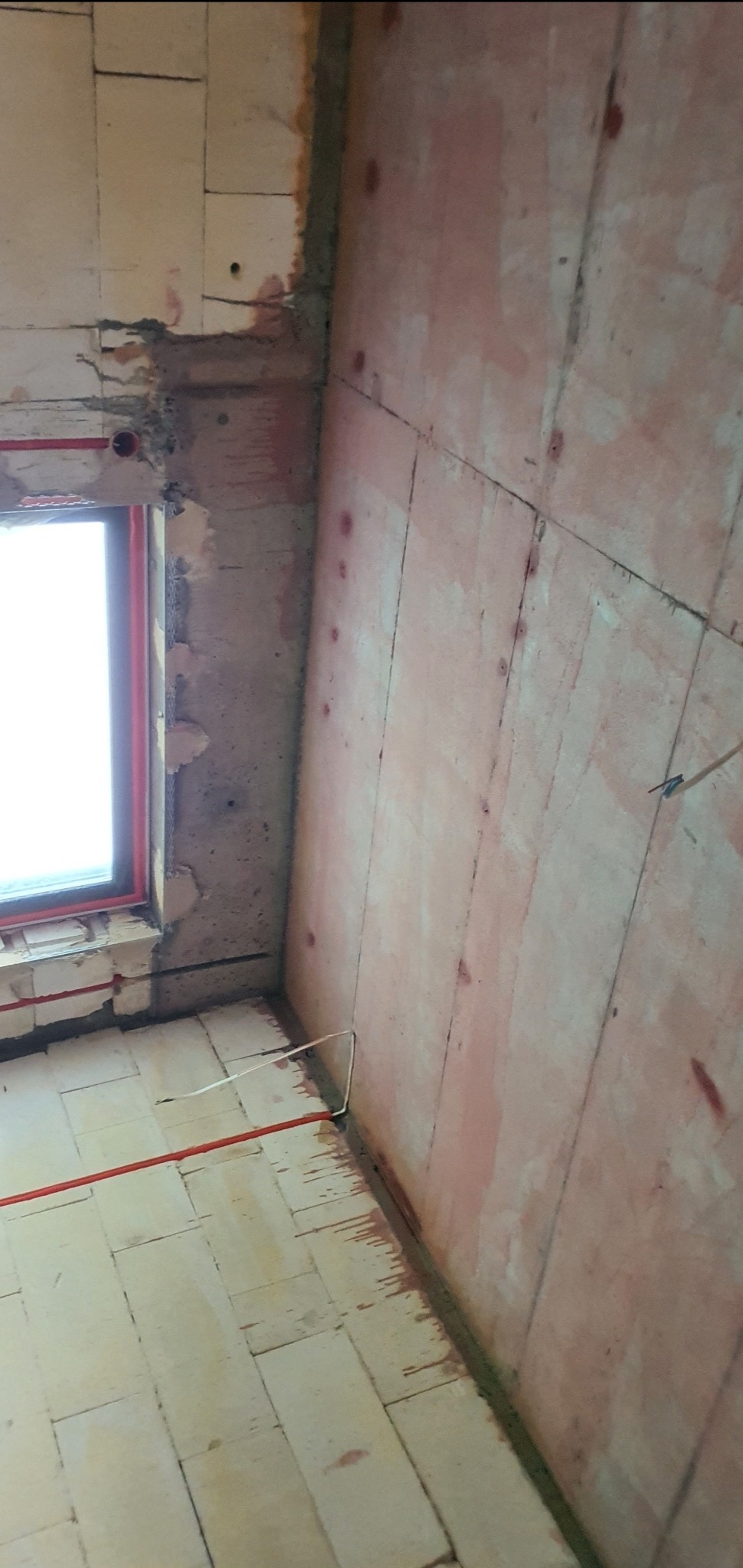 Wnętrze w trakcie prac: ściana z panelami przygotowana do nałożenia tynku, widoczne ślady po zaprawie i instalacjach.